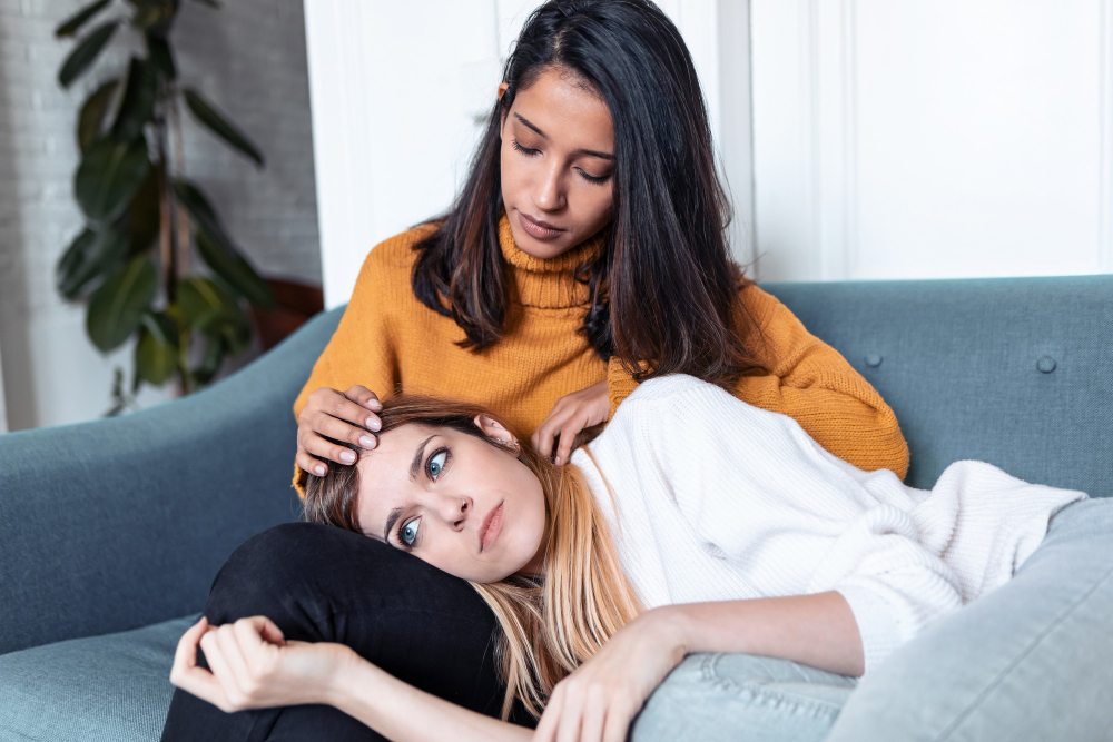 shot-pretty-young-woman-supporting-comforting-her-sad-friend-while-sitting-sofa-home